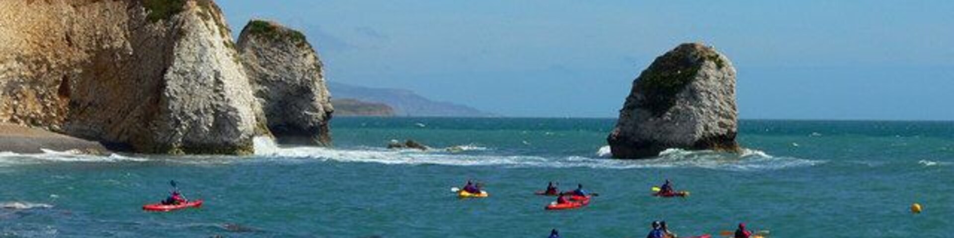 A coastal scene with kayakers on the water, cliffs, and large rock formations.