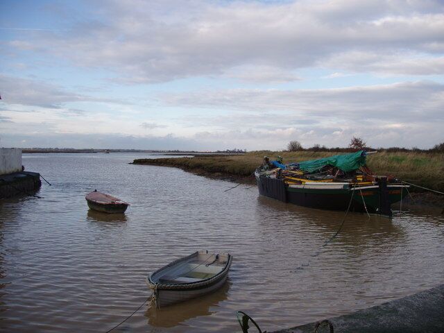 A calm river with boats, a small boat in the foreground, and a larger boat tied to the shore.
