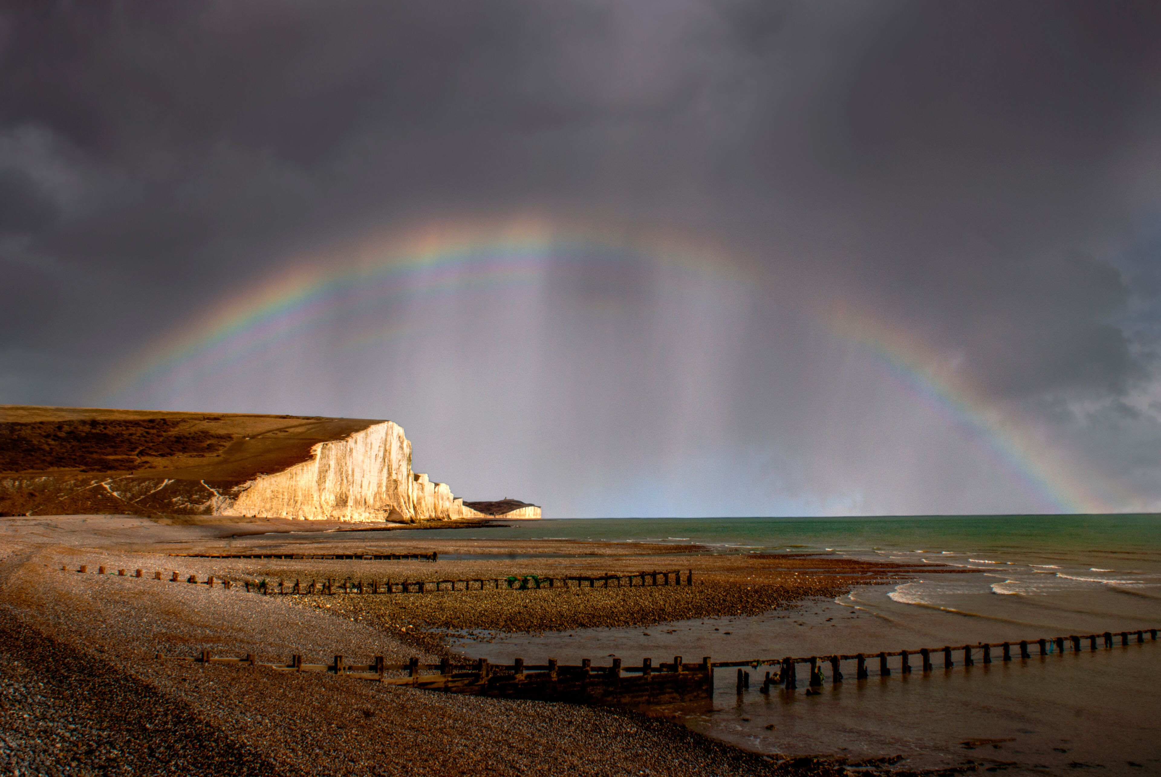 A beach with a cliff and a rainbow.