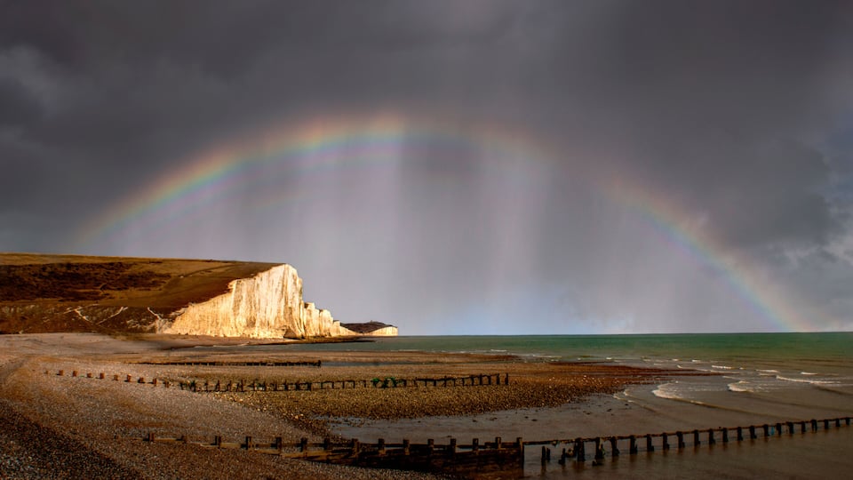 A beach with a cliff and a rainbow.