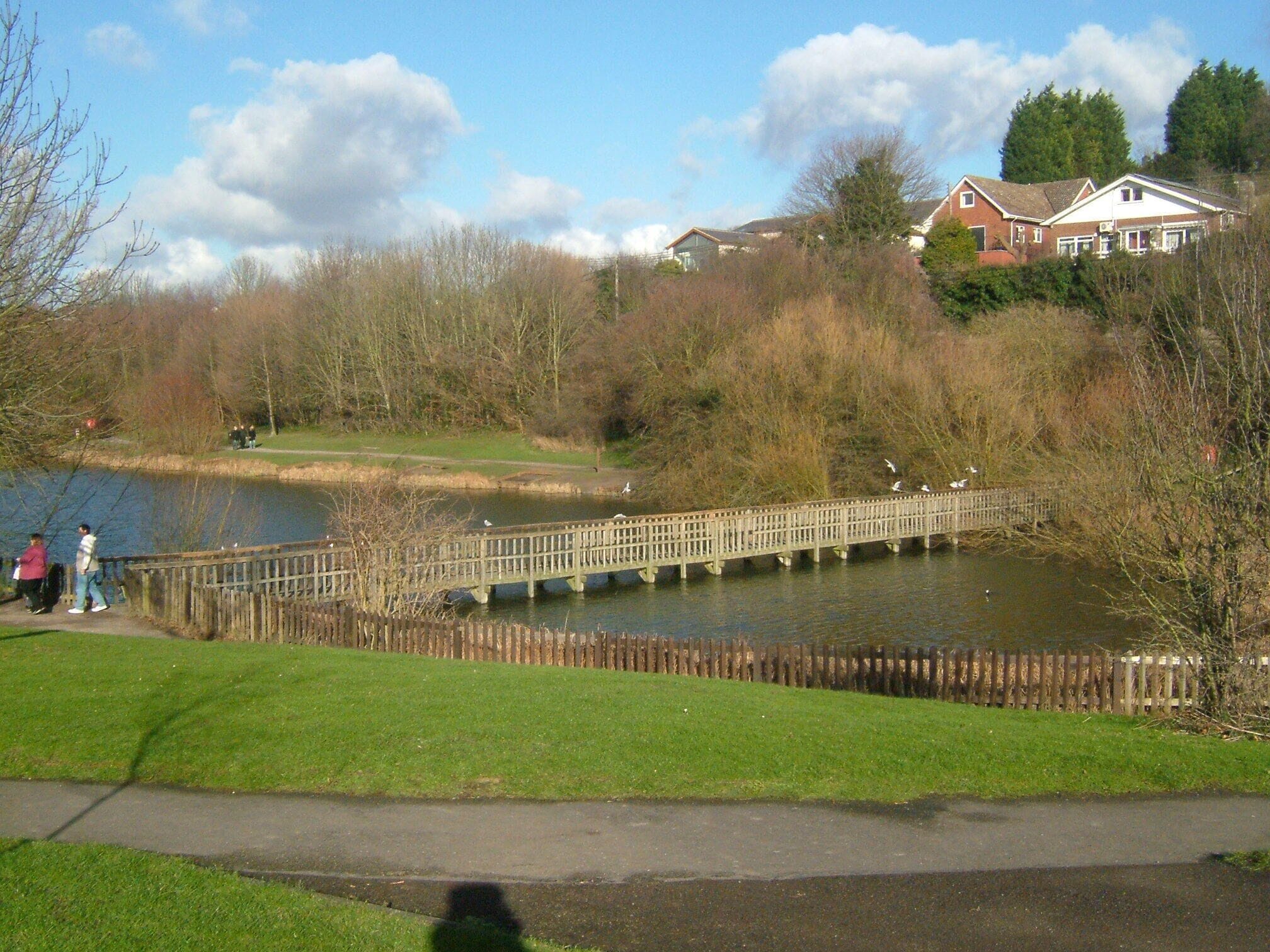 Un puente de madera sobre un lago, rodeado de árboles y casas.