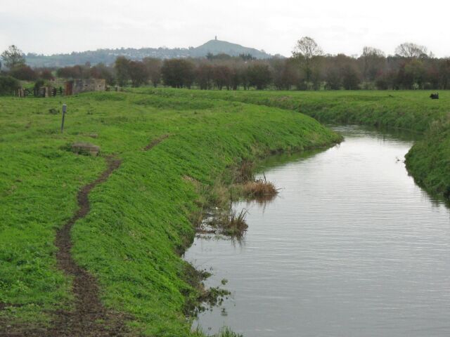 A narrow water channel with grassy banks, a path, and a distant hill.