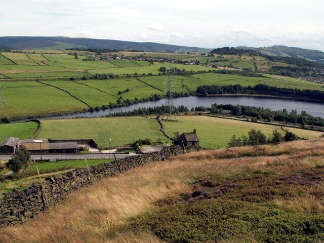 Paisaje rural con campos, un río y una pequeña construcción.