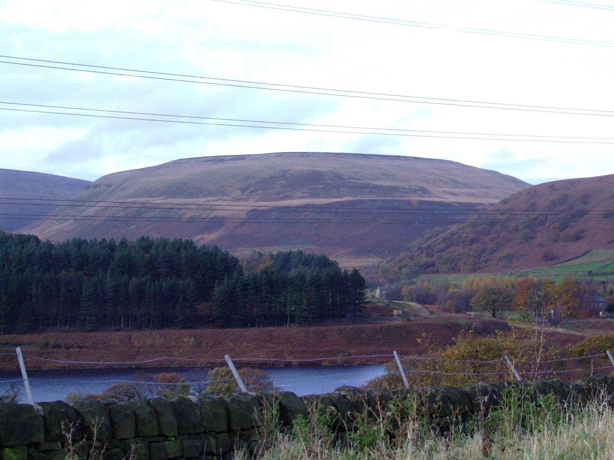 A valley with a river, stone wall, and forested hills.