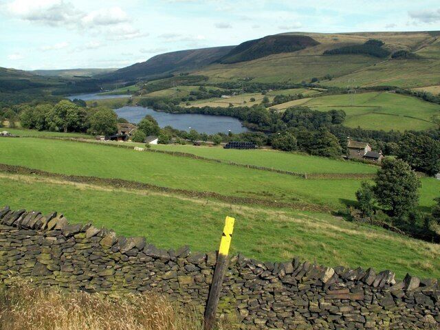 A rural landscape with a stone wall, a lake, and rolling hills.
