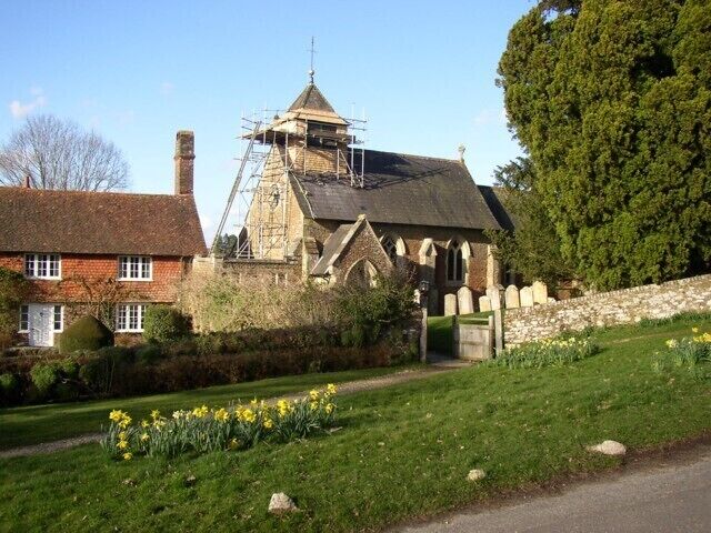 A church with scaffolding, a red brick house, and a garden with daffodils.
