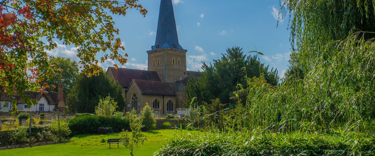 A church with a tall spire, surrounded by lush greenery and a clear blue sky.