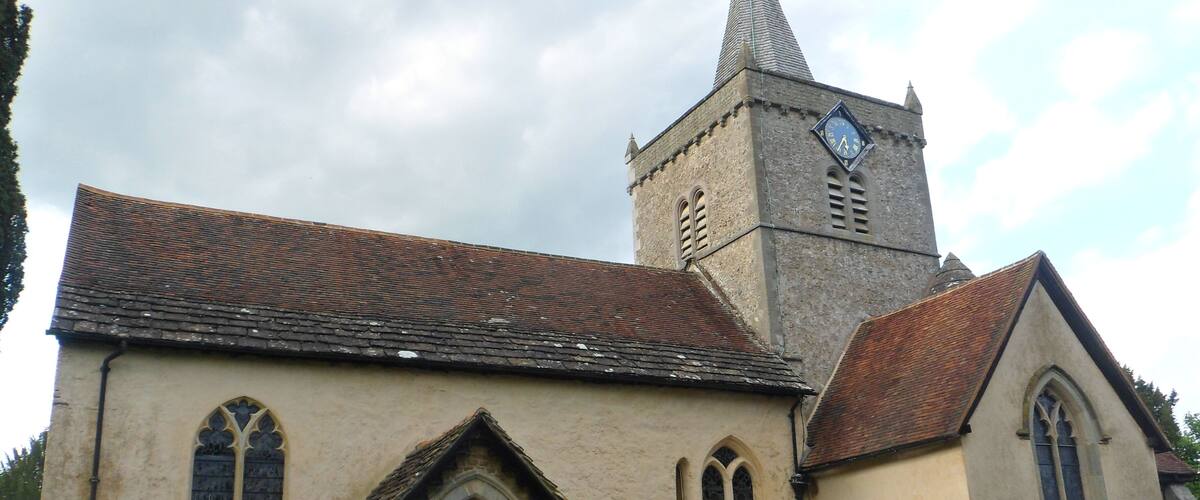 A church with a tall tower and a clock. There are gravestones in front of the building.