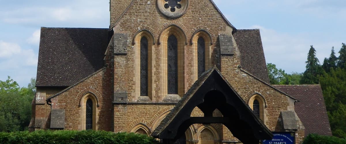 Een kerk met een hoge spits, gebogen ramen en een rond raam met glas-in-lood.