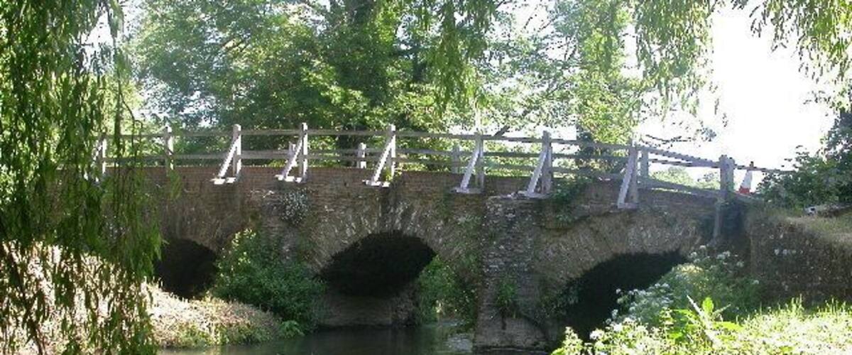 A stone bridge with three arches over a calm river, surrounded by lush greenery.