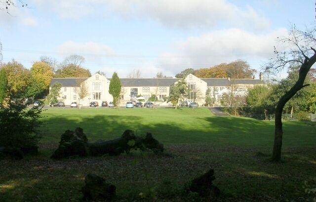 A large building with a lawn in front, surrounded by trees and parked cars.