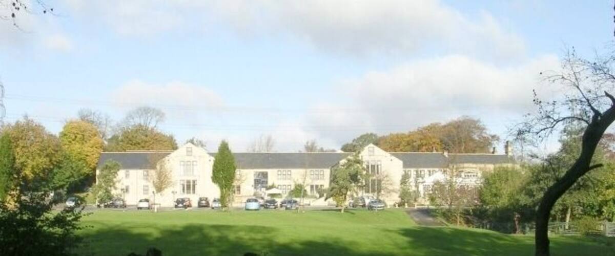 A large building with a lawn in front, surrounded by trees and parked cars.