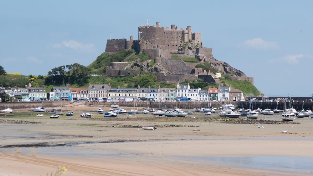 Une ville côtière qui abrite un château imposant perché sur une colline, une plage de sable et de nombreux bateaux amarrés le long de la côte.