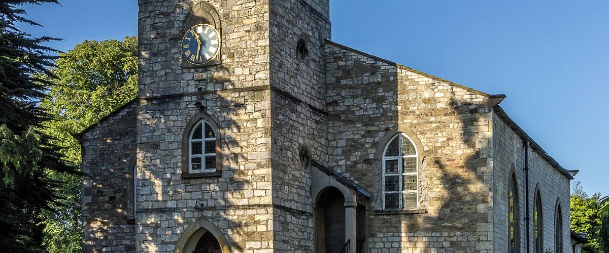 A stone church with a clock tower and a weather vane.
