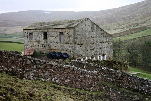 Barn in Sleddale A large barn with bales of silage and a trailer outside.