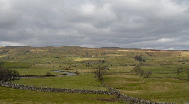 Rolling hills, a stone wall, and a river in a rural landscape.
