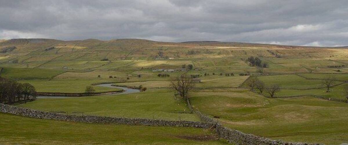 Rolling hills, a stone wall, and a river in a rural landscape.