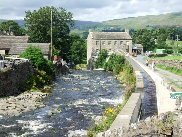 A river flowing through a rural area with stone walls and buildings.