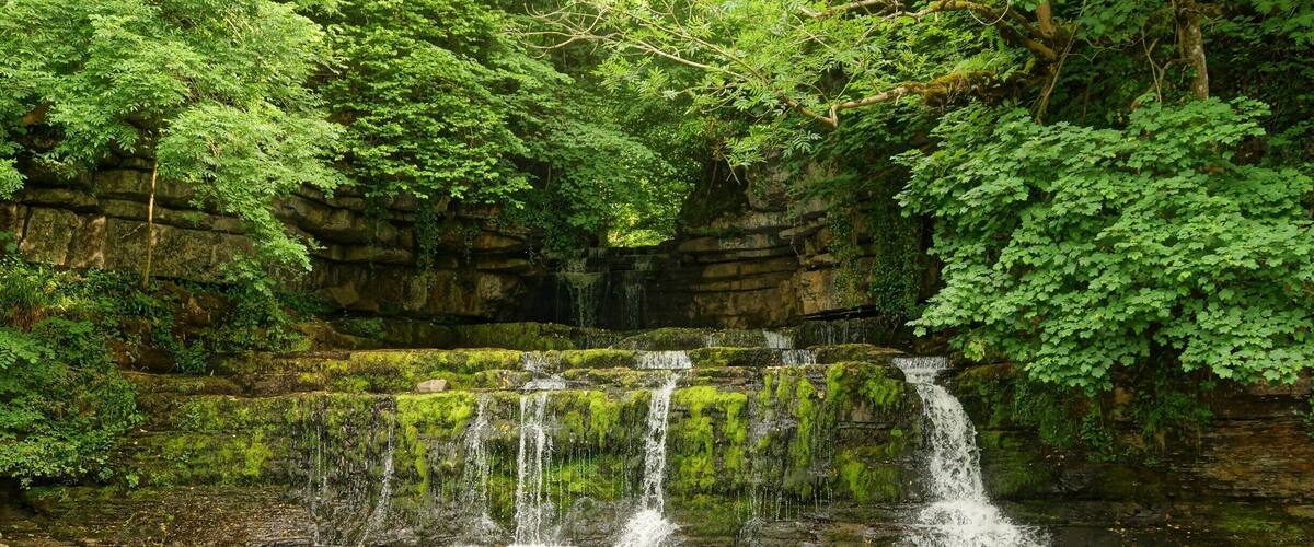 A multi-tiered waterfall cascading over moss-covered rocks into a clear pool.