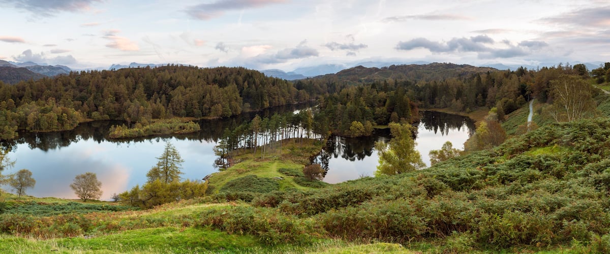Tyyni järvi, jonka ympärillä on tiheää metsää ja kumpuilevia kukkuloita.