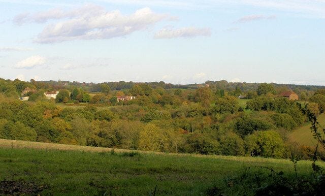 A rural landscape with rolling hills, scattered houses, and dense trees.