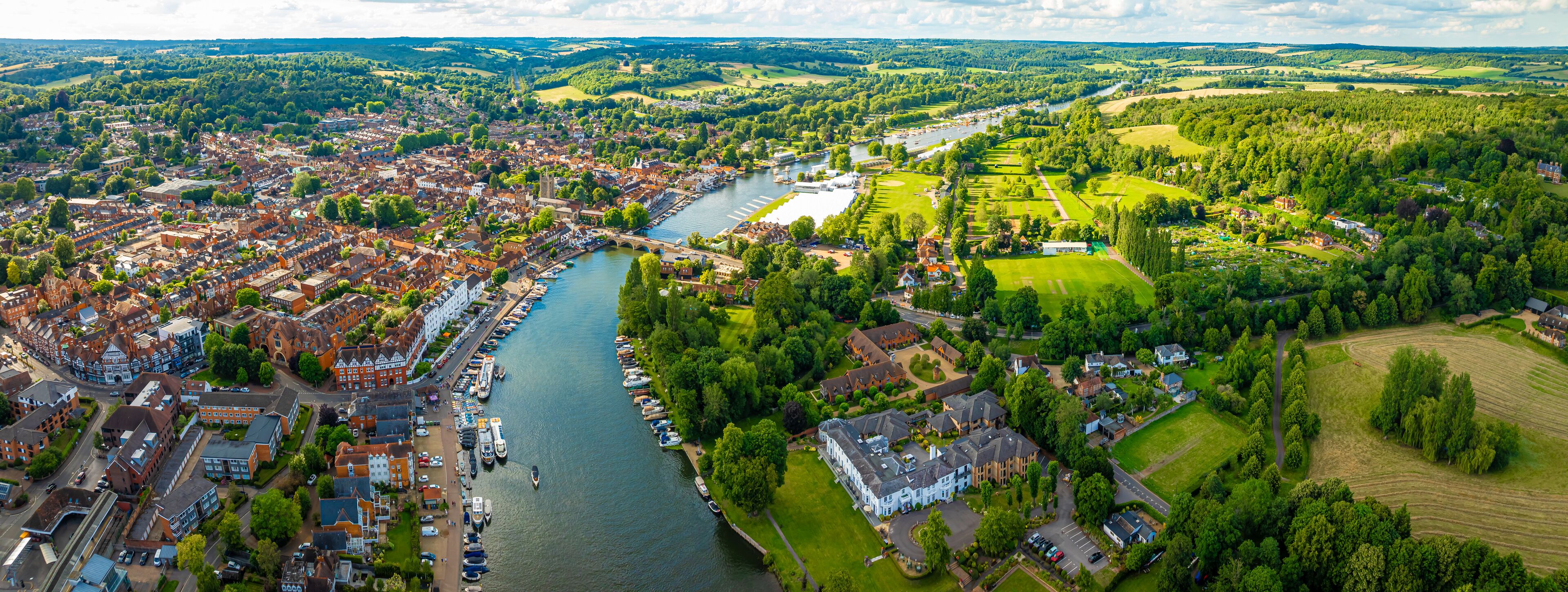 An aerial view of a riverside town with historic buildings, a river, and surrounding green fields.