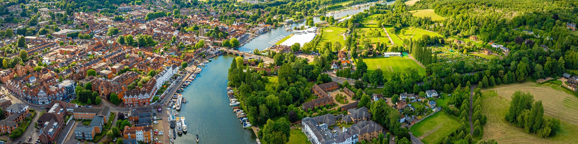 An aerial view of a riverside town with historic buildings, a river, and surrounding green fields.