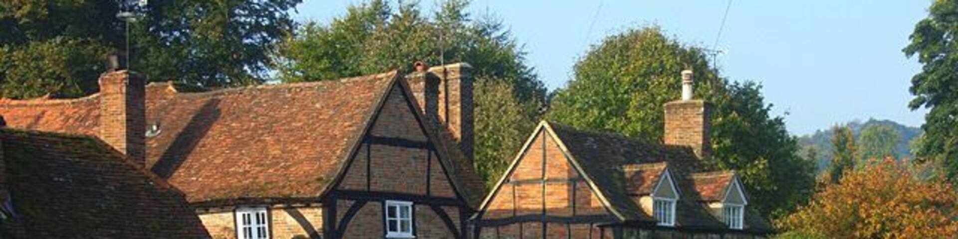 A traditional Tudor-style building with a thatched roof, surrounded by a well-maintained lawn and a stone wall.