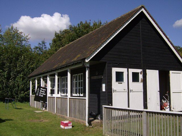 Reg Frewin Pavilion, Greys Green Cricket Club, Rotherfield Greys, Oxfordshire. The groundsman preparing for an afternoon's match is bringing out the sign stating that this is Greys Green Cricket Club.