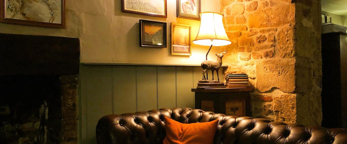 A cozy room with a leather sofa, a lamp, and framed artwork on the wall.