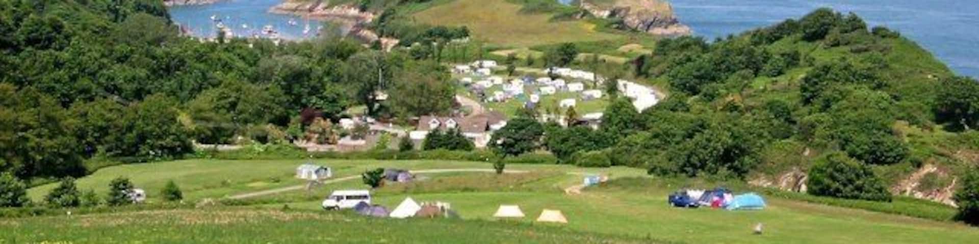A coastal village with green hills, tents, and a clear view of the sea.