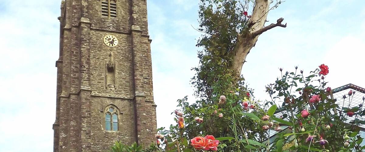 A stone tower with a clock, surrounded by lush greenery and flowering plants.