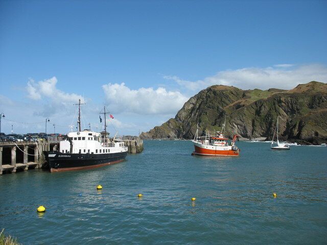 A harbor with two boats, a rocky coastline, and a clear sky.