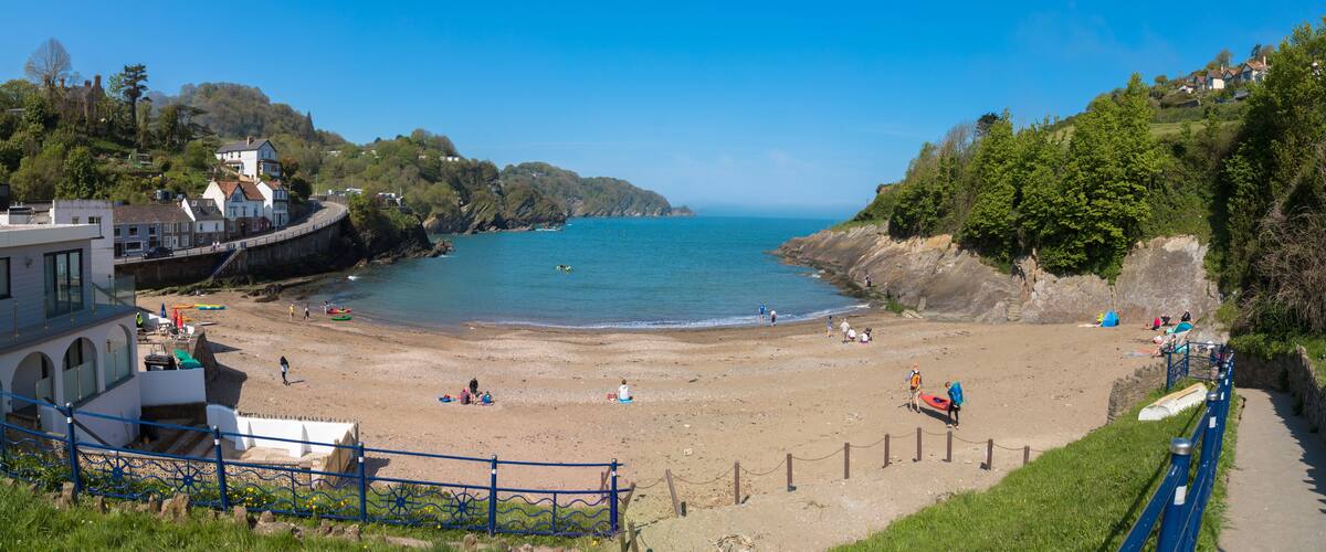 A coastal beach with people, kayaks, and a clear blue sky.
