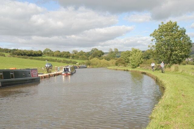 A narrow canal with boats docked on the left, surrounded by grassy banks and trees.