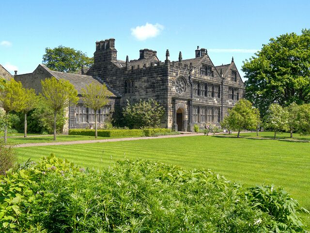 A large stone building with a clock tower, surrounded by a well-maintained lawn and trees.