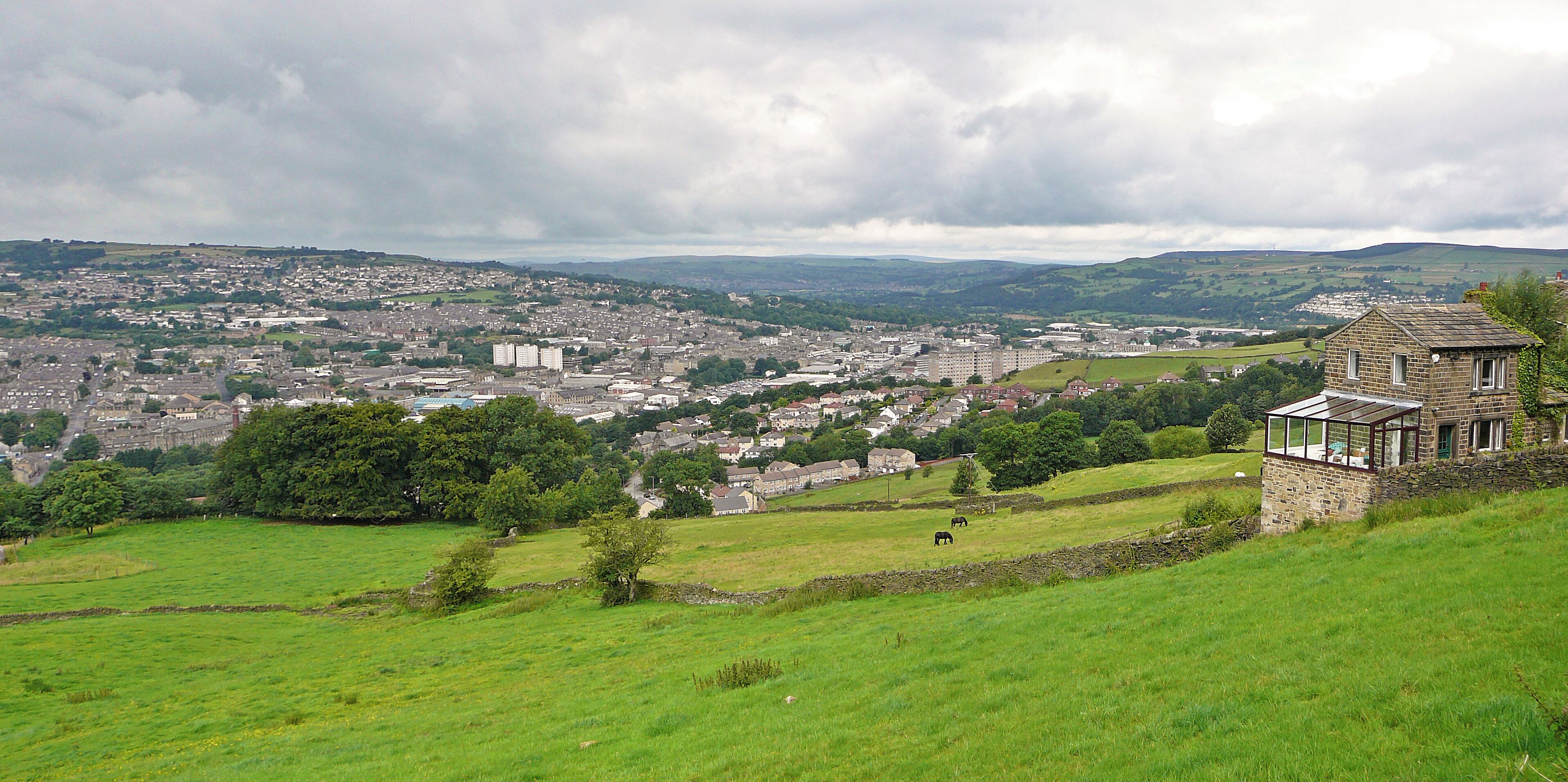 A rural landscape with a stone house, green fields, and a distant town.
