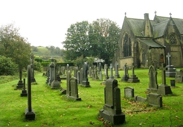 A cemetery with numerous gravestones and a church in the background.