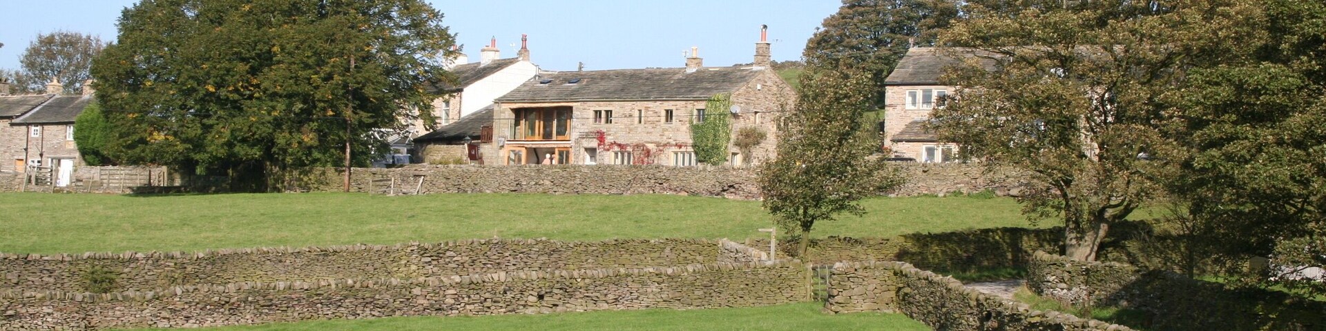 Un paysage rural caractérisé par des murs de pierre, un grand arbre et des maisons traditionnelles en pierre.