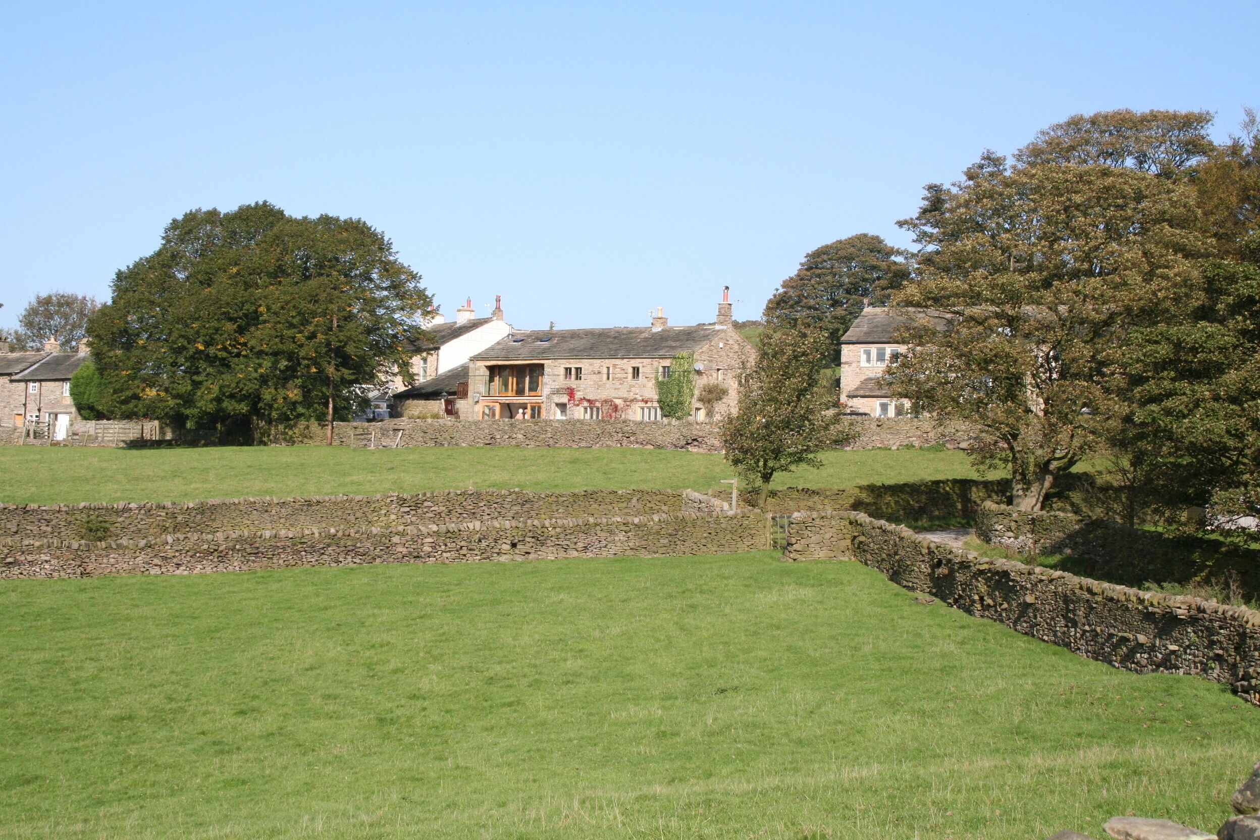 A rural landscape with stone walls, a large tree, and traditional stone houses.