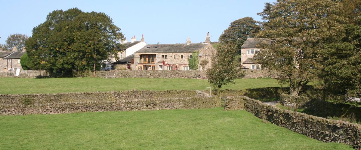 A rural landscape with stone walls, a large tree, and traditional stone houses.