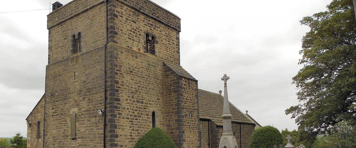 A historic stone church with a tall tower, a cross at the front, and a cemetery with gravestones.