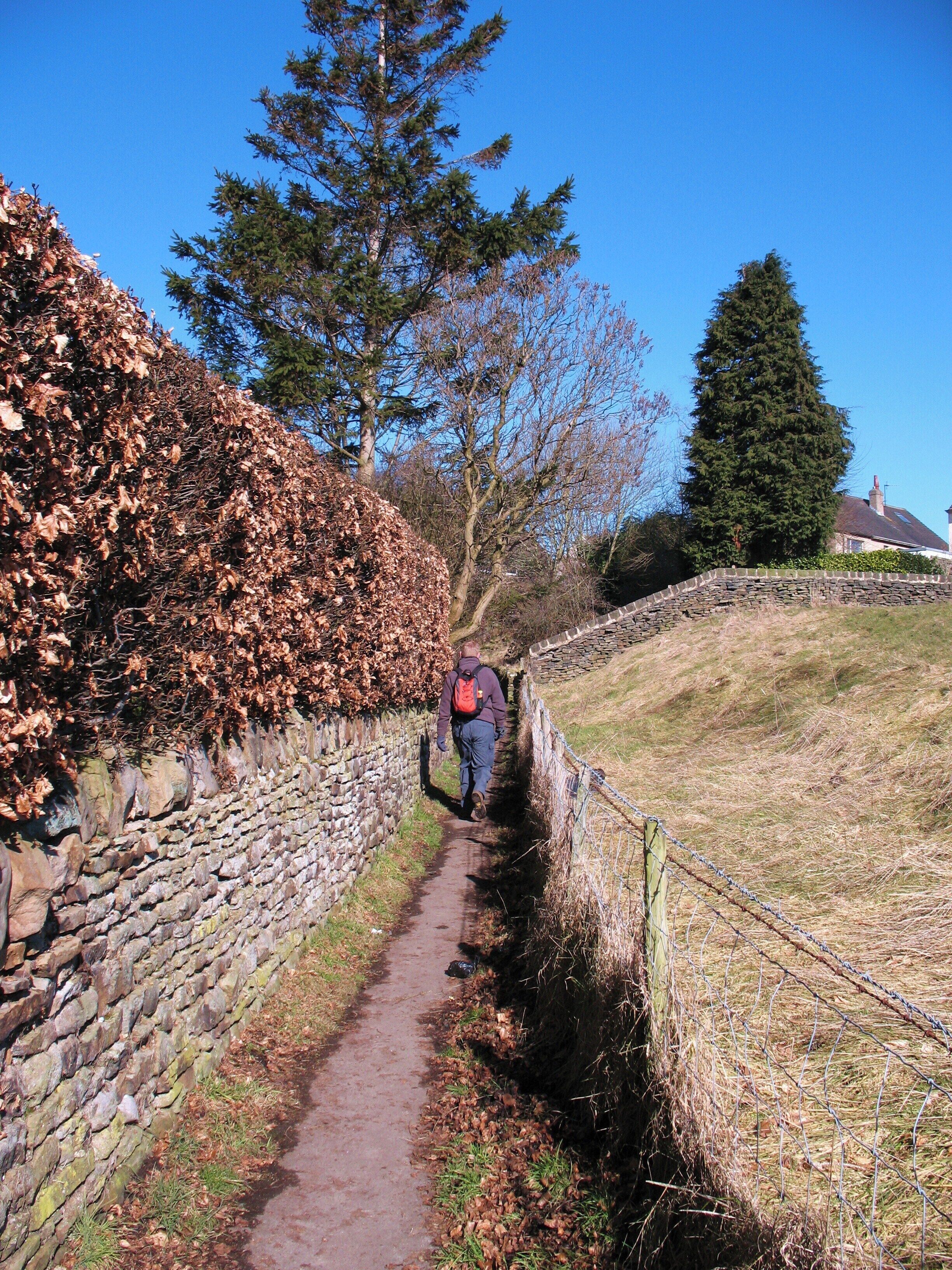 A narrow stone path with a hiker wearing a backpack.