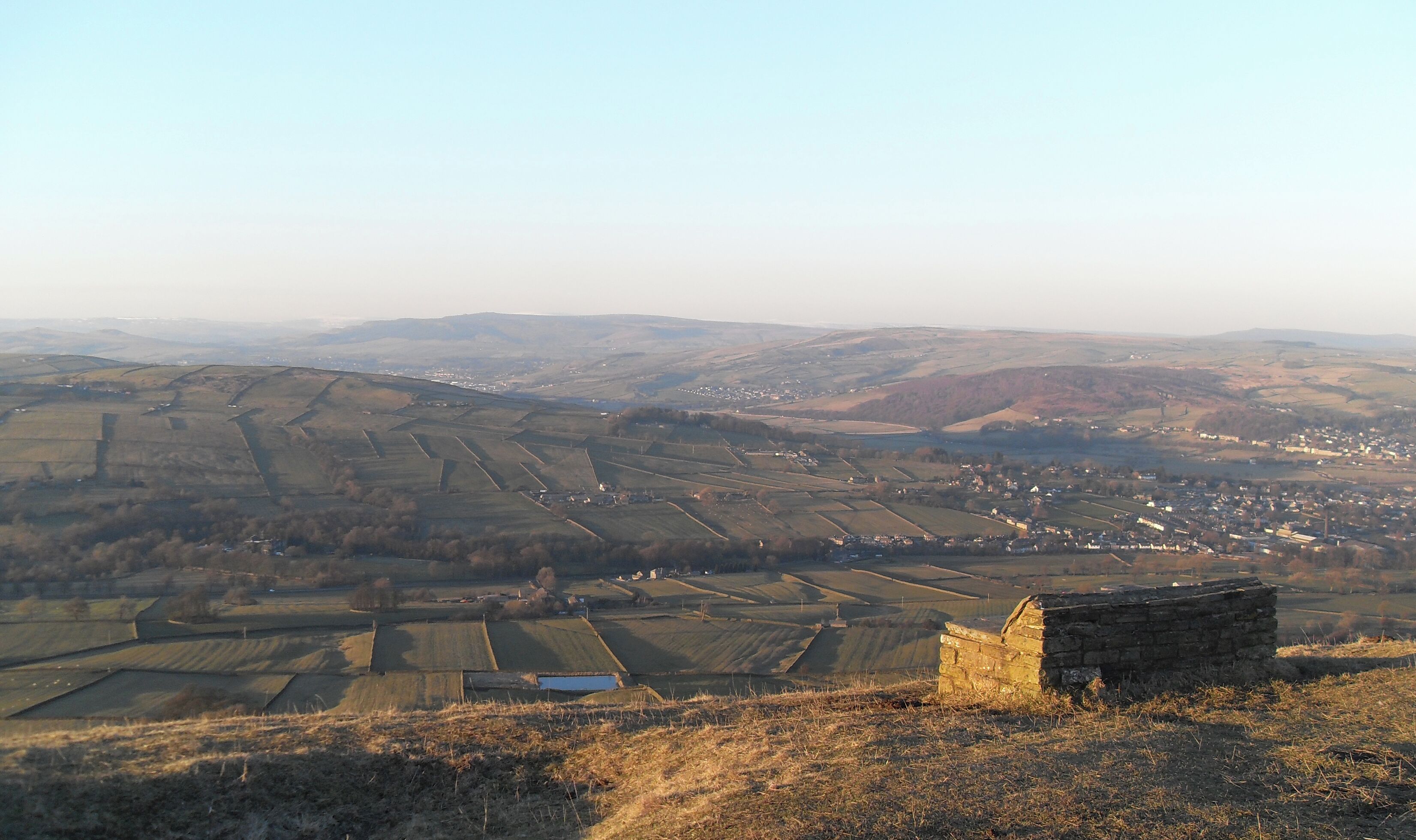 A rural landscape with terraced fields, a small stone structure, and a distant village.