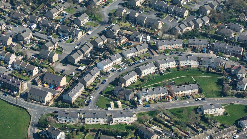 An aerial view of a residential area with houses, roads, and green spaces.