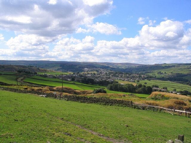 Rolling green hills, a stone wall, and a distant village.
