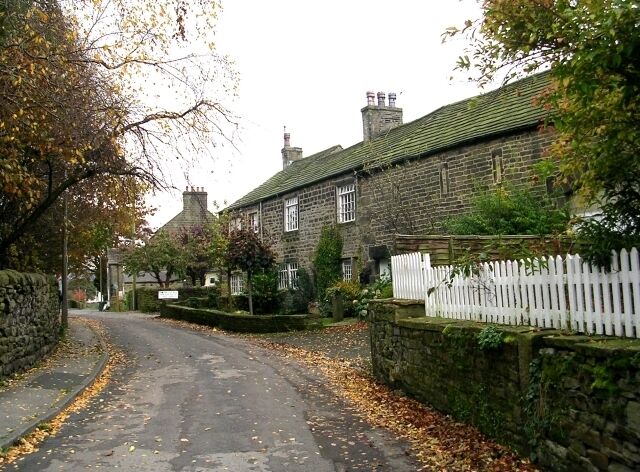 A narrow cobblestone street flanked by stone houses with white picket fences.