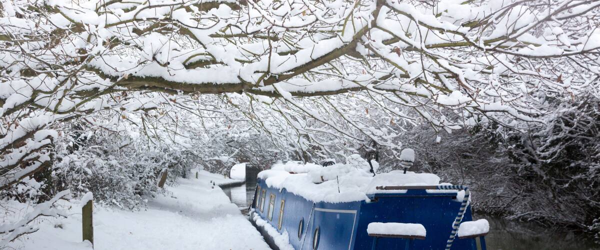 A snow-covered boat docked by a snowy riverbank.