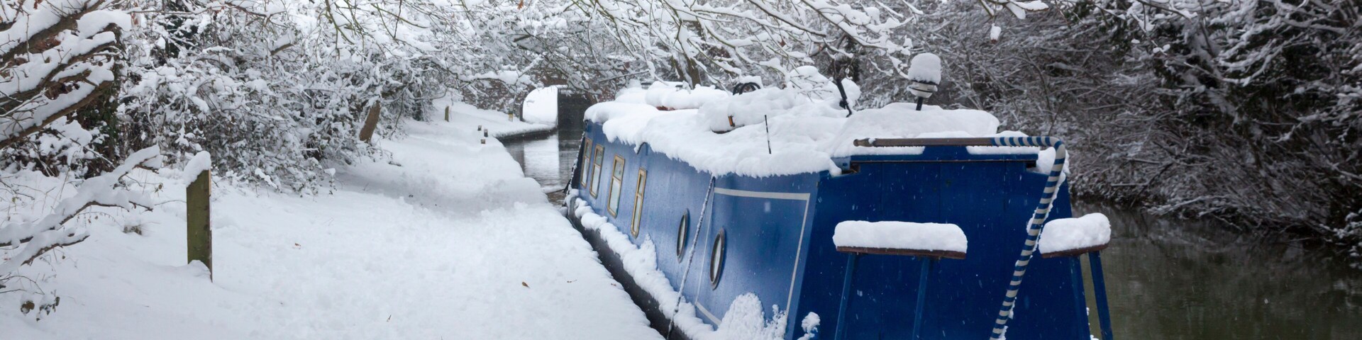 A snow-covered boat docked by a snowy riverbank.