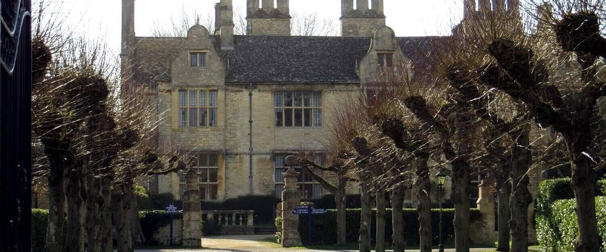 A historic building with a symmetrical facade, a central entrance, and a well-maintained garden with trees and a gravel path.